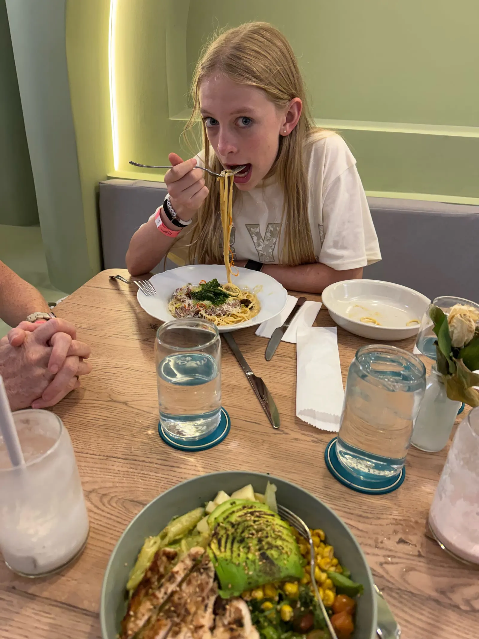Eliza twirling a big forkful of spaghetti at lunch, with a chicken and avocado bowl in the foreground.