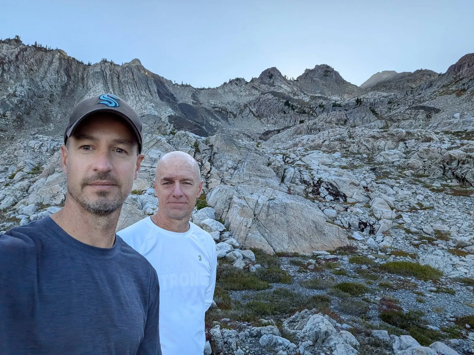 Daniel and me in a selfie among pale rock slabs and low alpine plants, with jagged ridges behind us in the evening light.